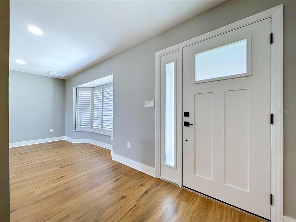 An entryway features light wood flooring, gray walls, a white front door, and a bay window — 381 WESTWINDS DRIVE, PALM HARBOR, FL