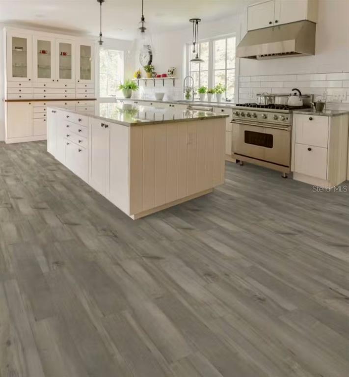 A modern kitchen features white cabinetry, a large central island, and gray wood-look flooring — 6873 SUNDIAL DRIVE, LAKELAND, FL