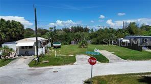 An empty corner lot with a small house and a stop sign in the foreground — 6981 EDGEWATER DRIVE, NEW PORT RICHEY, FL