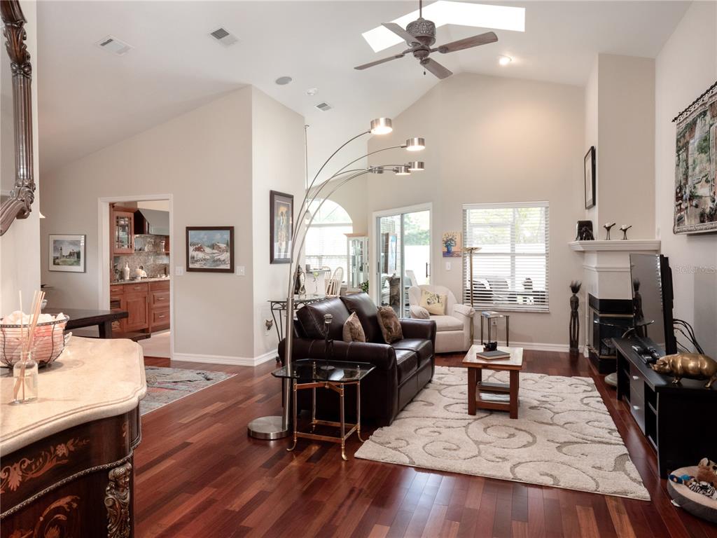 A living room with hardwood floors, a vaulted ceiling, a fireplace, and a leather sofa — 6126 NW 36TH DRIVE, GAINESVILLE, FL