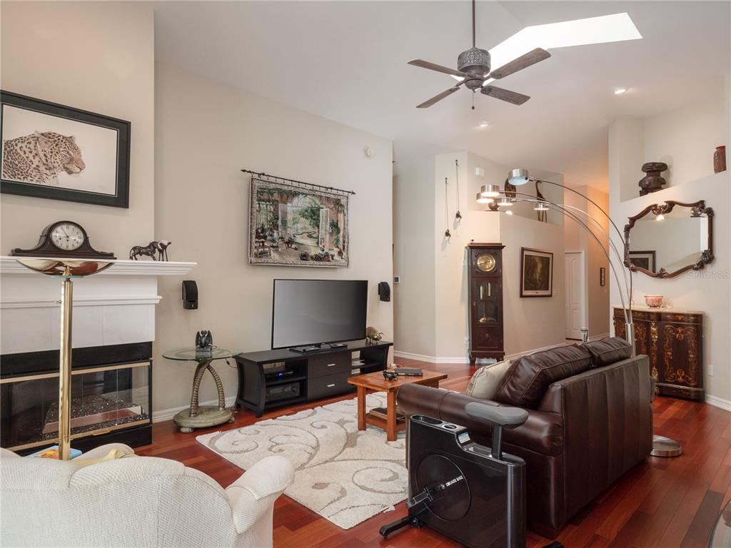 A living room with a fireplace, television, leather sofa, exercise bike, and hardwood flooring — 6126 NW 36TH DRIVE, GAINESVILLE, FL