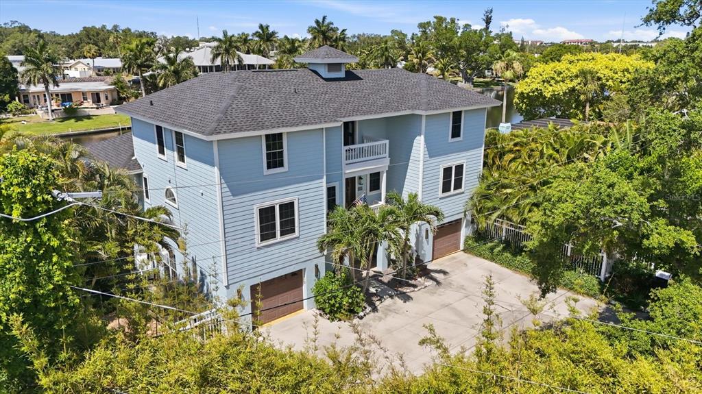 An elevated three-story light blue house with a dark shingled roof and two garage doors — 5544 DINAH LANE, SARASOTA, FL
