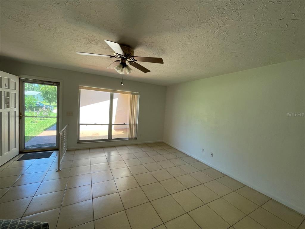 A living room with light-colored tile flooring, a ceiling fan, and a large window — 12 FARRADAY LANE UNIT A, PALM COAST, FL