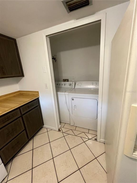 A laundry closet with a washer and dryer sits beside wooden cabinets and tiled floors — 12 FARRADAY LANE UNIT A, PALM COAST, FL