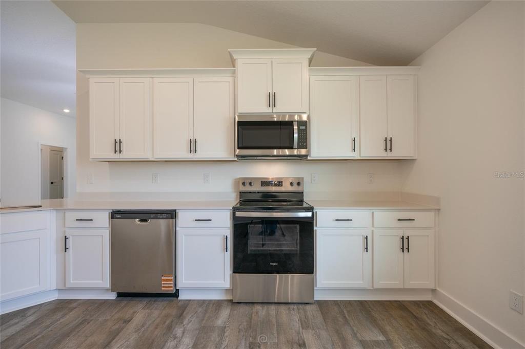 A kitchen features white cabinets, stainless steel appliances, and wood-look flooring — 32 RYMSHAW DRIVE, PALM COAST, FL