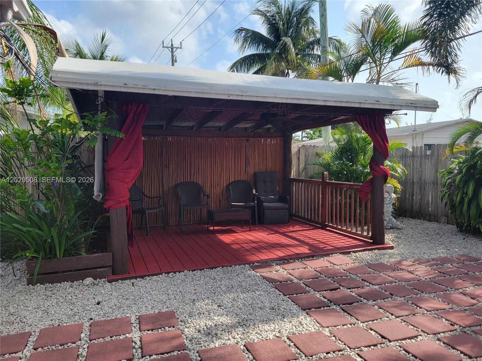 A covered wooden deck with red flooring, bamboo walls, and patio furniture in a backyard — 2560 NE 8th Ter, Pompano Beach FL 33064, POMPANO BEACH, FL