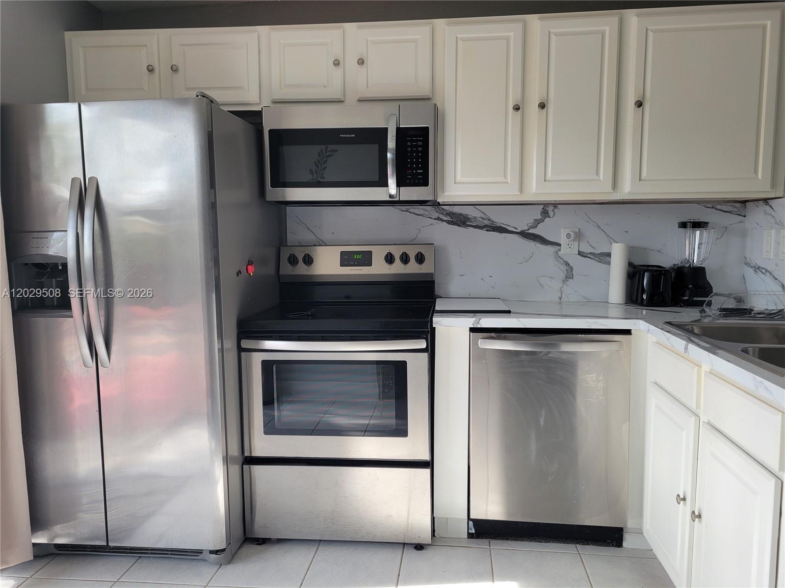 A kitchen features white cabinets, stainless steel appliances, and a marble-patterned backsplash — 2560 NE 8th Ter, Pompano Beach FL 33064, POMPANO BEACH, FL