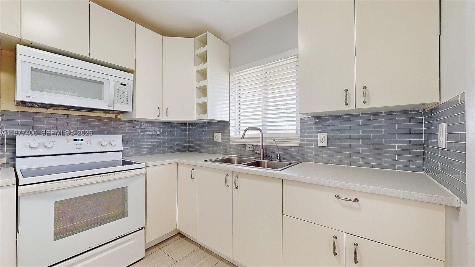 A kitchen features white cabinets, a white stove, a microwave, and a gray tiled backsplash — 5300 Washington St # D303, Hollywood FL 33021, HOLLYWOOD, FL
