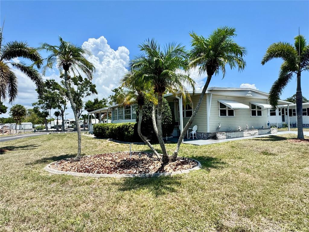 A light-colored mobile home sits on a grassy lot with several palm trees — 5511 DENMARK DRIVE, BRADENTON, FL