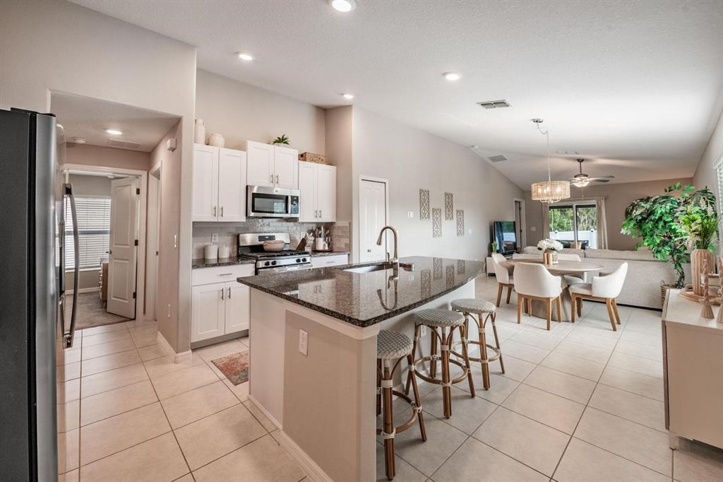 A kitchen with white cabinets, granite countertops, and a center island with three bar stools — 10331 BLUE PLUME COURT, RIVERVIEW, FL