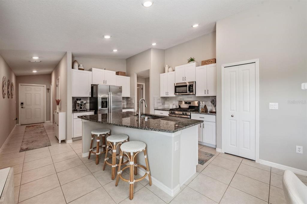 A kitchen with white cabinets, granite countertops, a center island with stools, and tile flooring — 10331 BLUE PLUME COURT, RIVERVIEW, FL