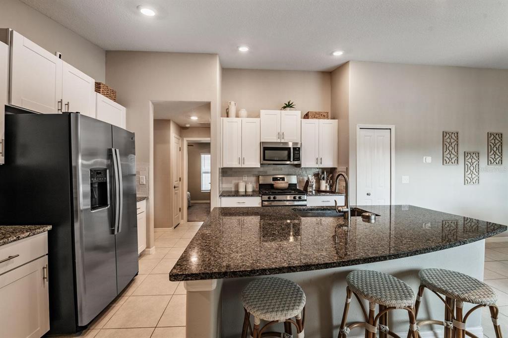 A kitchen with white cabinets, stainless steel appliances, granite countertops, and a breakfast bar — 10331 BLUE PLUME COURT, RIVERVIEW, FL