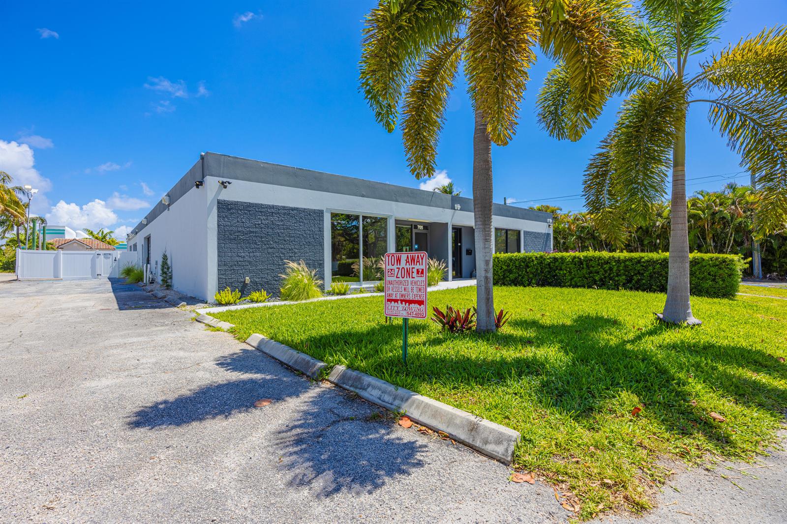 A single-story commercial building with a gray facade sits behind a lawn and palm trees — 705 Bond Way, Delray Beach FL 33483, DELRAY BEACH, FL