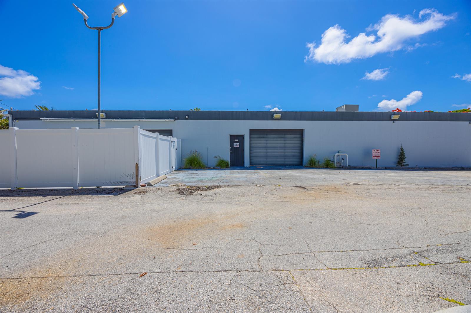 A gray commercial building with a roll-up door, a single entry door, and a parking lot — 705 Bond Way, Delray Beach FL 33483, DELRAY BEACH, FL
