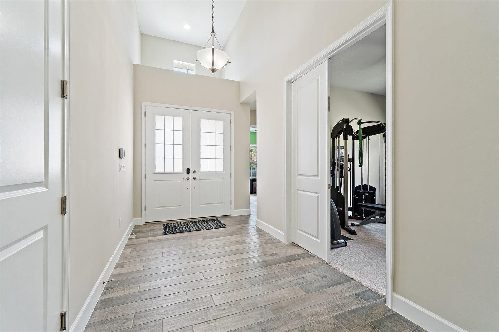 An entryway with light wood-look tile flooring, a high ceiling, and a home gym room — 15955 Whippoorwill Circle, Westlake FL 33470, WESTLAKE, FL