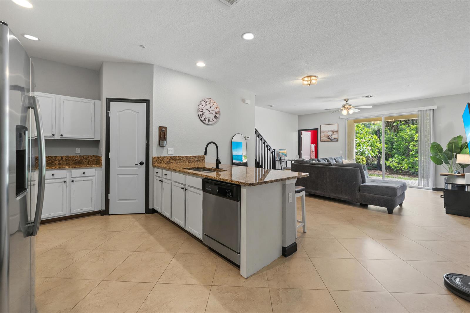 An open-concept kitchen with white cabinets and granite countertops overlooks a living room with tile floors — 3051 SW Otter Lane, Stuart FL 34997, STUART, FL