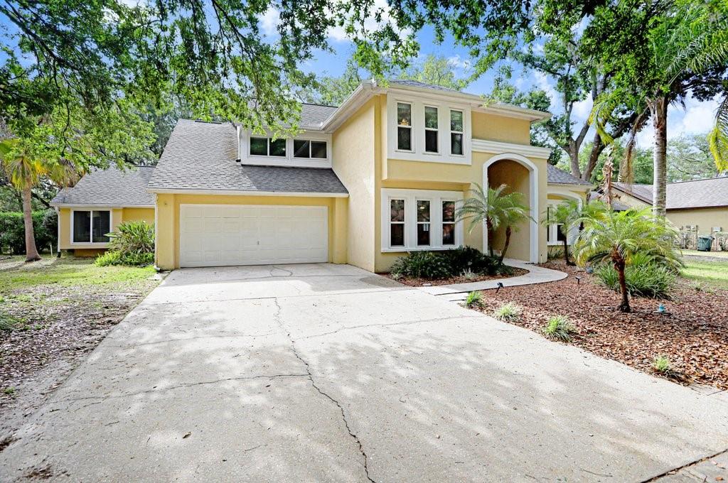 A two-story yellow house with a concrete driveway, a two-car garage, and mature trees — 6214 FARTHING STREET, TAMPA, FL