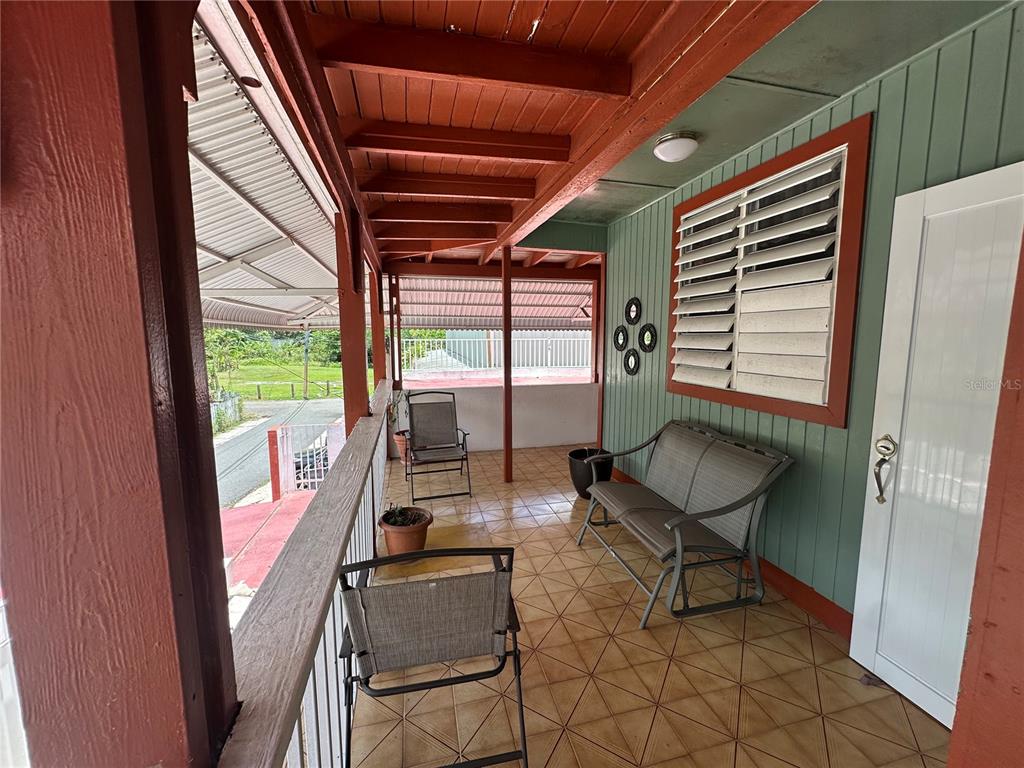 A covered porch features tiled flooring, outdoor furniture, and a green-sided wall with shutters — calle 5 COMUNIDAD RURAL VILLA BORINQUEN, CANOVANAS, PR