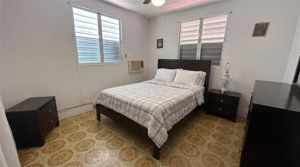 A bedroom features a bed, two nightstands, patterned tile flooring, and two louvered windows — calle 5 COMUNIDAD RURAL VILLA BORINQUEN, CANOVANAS, PR