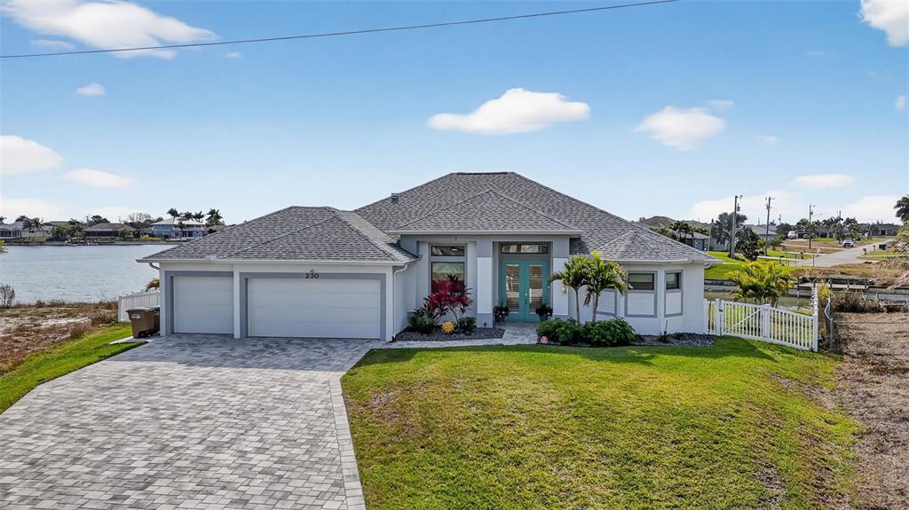 A single-story house with a gray roof, light siding, and a paved driveway faces water — 230 NE 18TH STREET, CAPE CORAL, FL