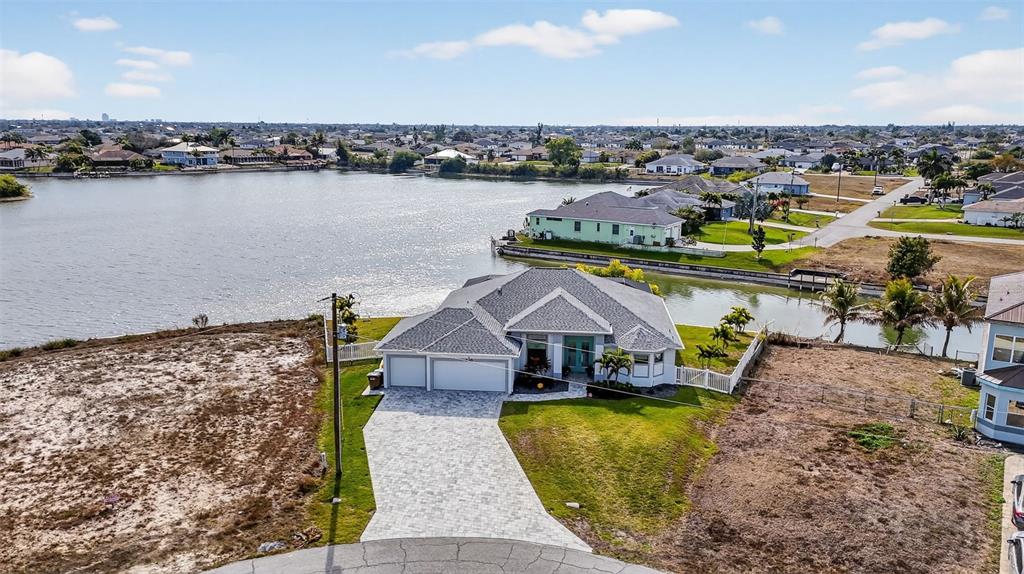 An aerial view shows a single-story house with a paved driveway and a waterfront backyard — 230 NE 18TH STREET, CAPE CORAL, FL