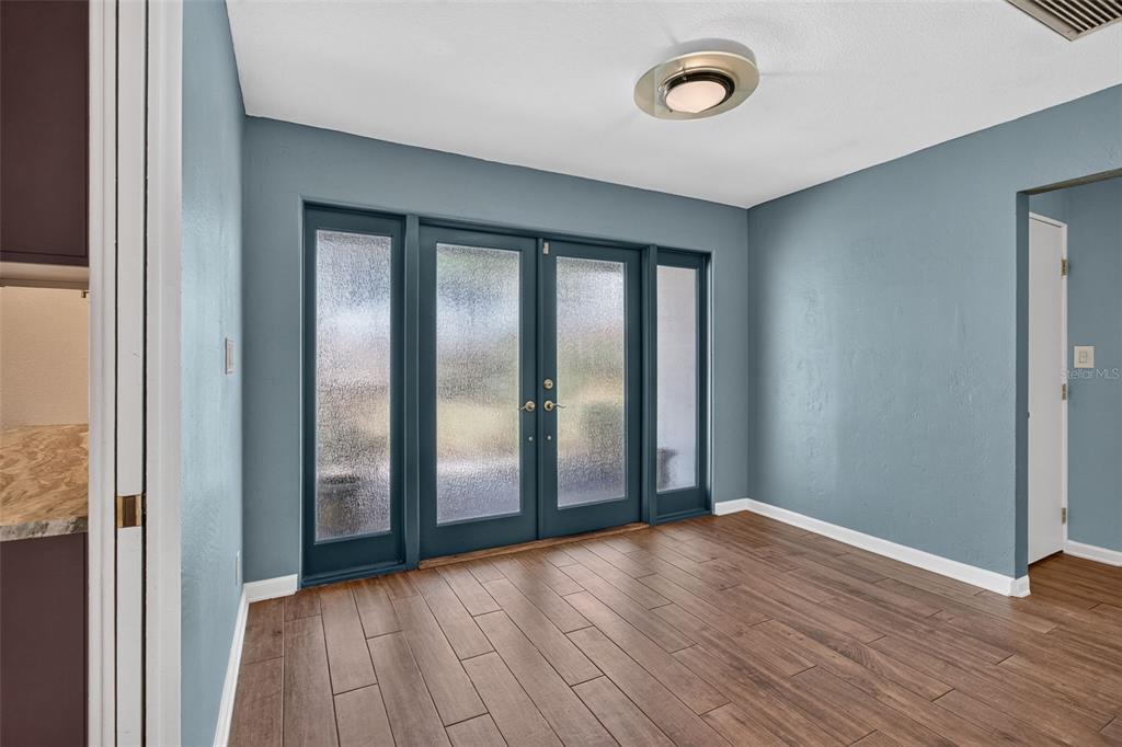 A dining room with blue walls, wood-look tile flooring, and a set of glass-paneled doors — 8094 12TH AVENUE S, ST PETERSBURG, FL