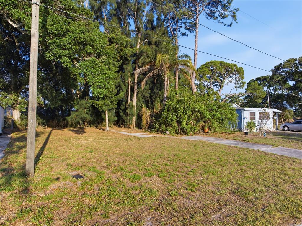 A vacant, grassy residential lot features a concrete driveway and mature trees in the background — 61ST LANE, PINELLAS PARK, FL