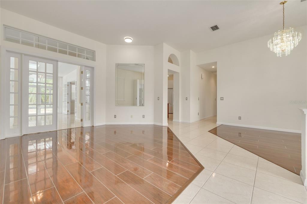 A bright room features polished wood-look tile flooring, white walls, and a crystal chandelier — 3713 SIENA LANE, PALM HARBOR, FL