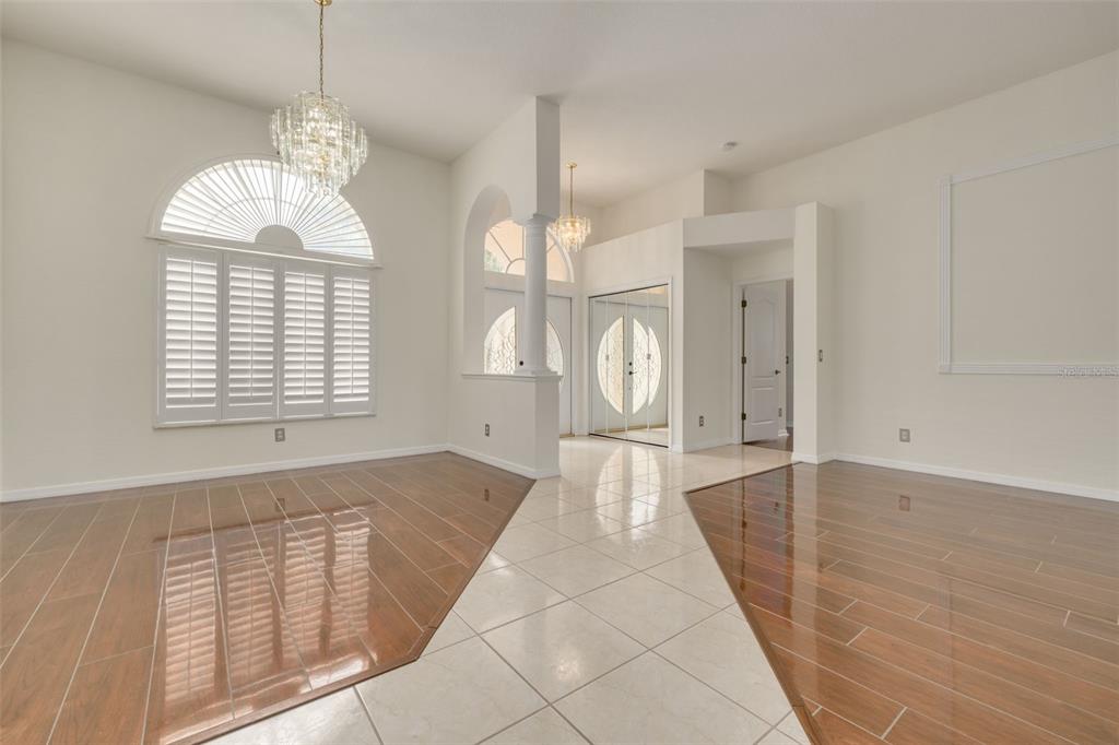 An entryway and dining area feature glossy wood-look tile floors and a large crystal chandelier — 3713 SIENA LANE, PALM HARBOR, FL