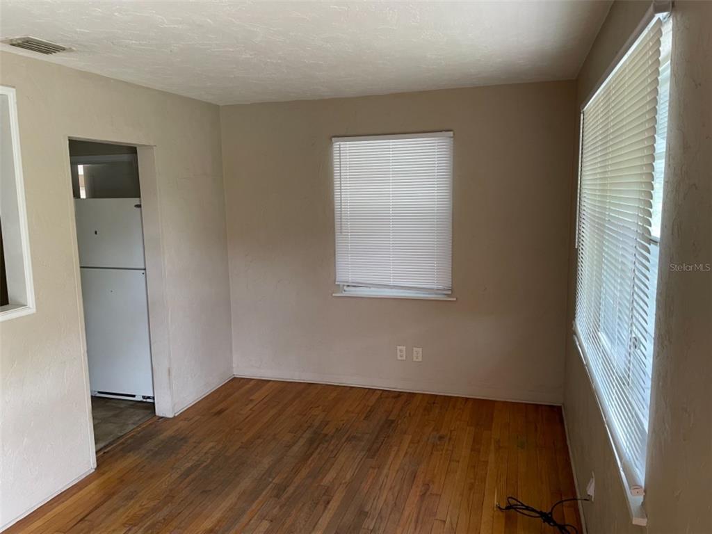 An empty room with hardwood floors, two windows with blinds, and a view into a kitchen — 5013 20TH STREET N, ST PETERSBURG, FL