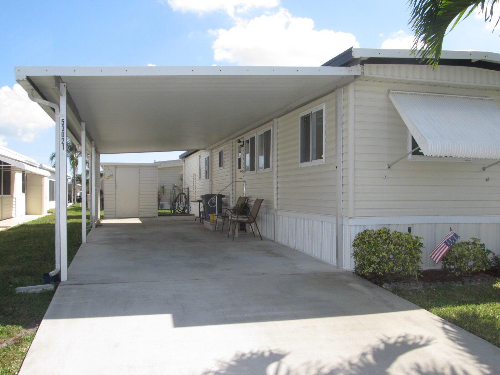 A mobile home exterior features a large concrete carport, a storage shed, and light-colored siding — 53021 Del Rio Bay, Boynton Beach FL 33436, BOYNTON BEACH, FL