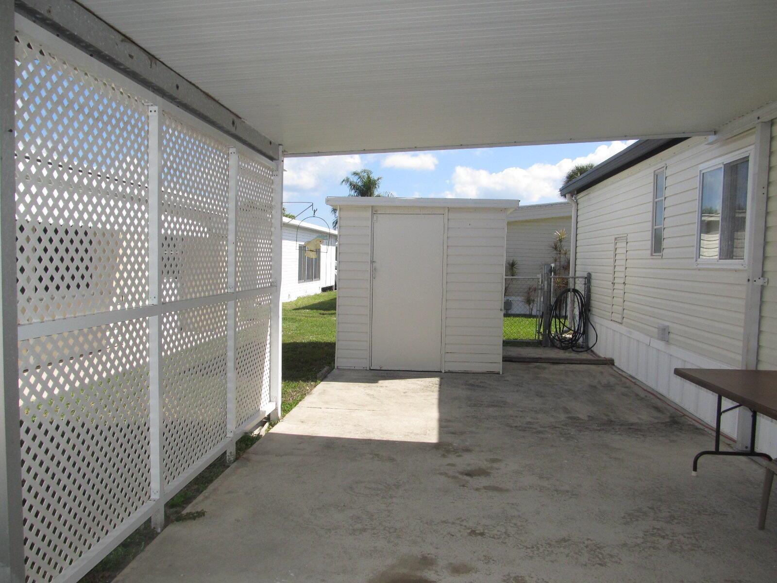 A concrete carport features a white lattice privacy screen, a storage shed, and a table — 53021 Del Rio Bay, Boynton Beach FL 33436, BOYNTON BEACH, FL