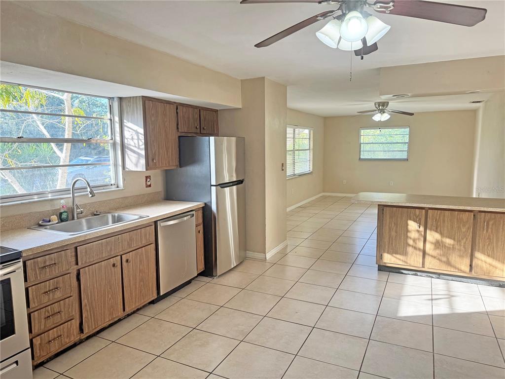 A kitchen with wood cabinets, stainless steel appliances, and tile flooring opens to a dining area — 12438 POEM AVENUE, PUNTA GORDA, FL