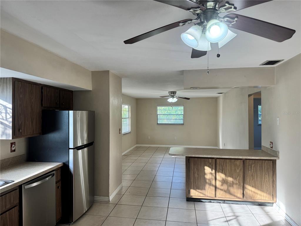 A kitchen with stainless steel appliances and wood cabinets opens into a tiled living area — 12438 POEM AVENUE, PUNTA GORDA, FL
