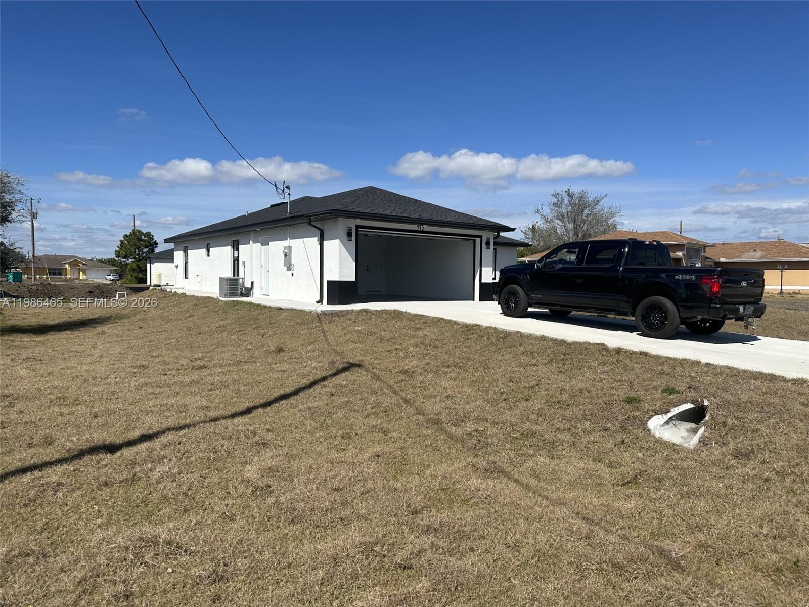 A white house with a black roof and an open garage sits on a grassy lot — 712 EUSTON AVENUE S, Lehigh Acres FL 33974, LEHIGH ACRES, FL