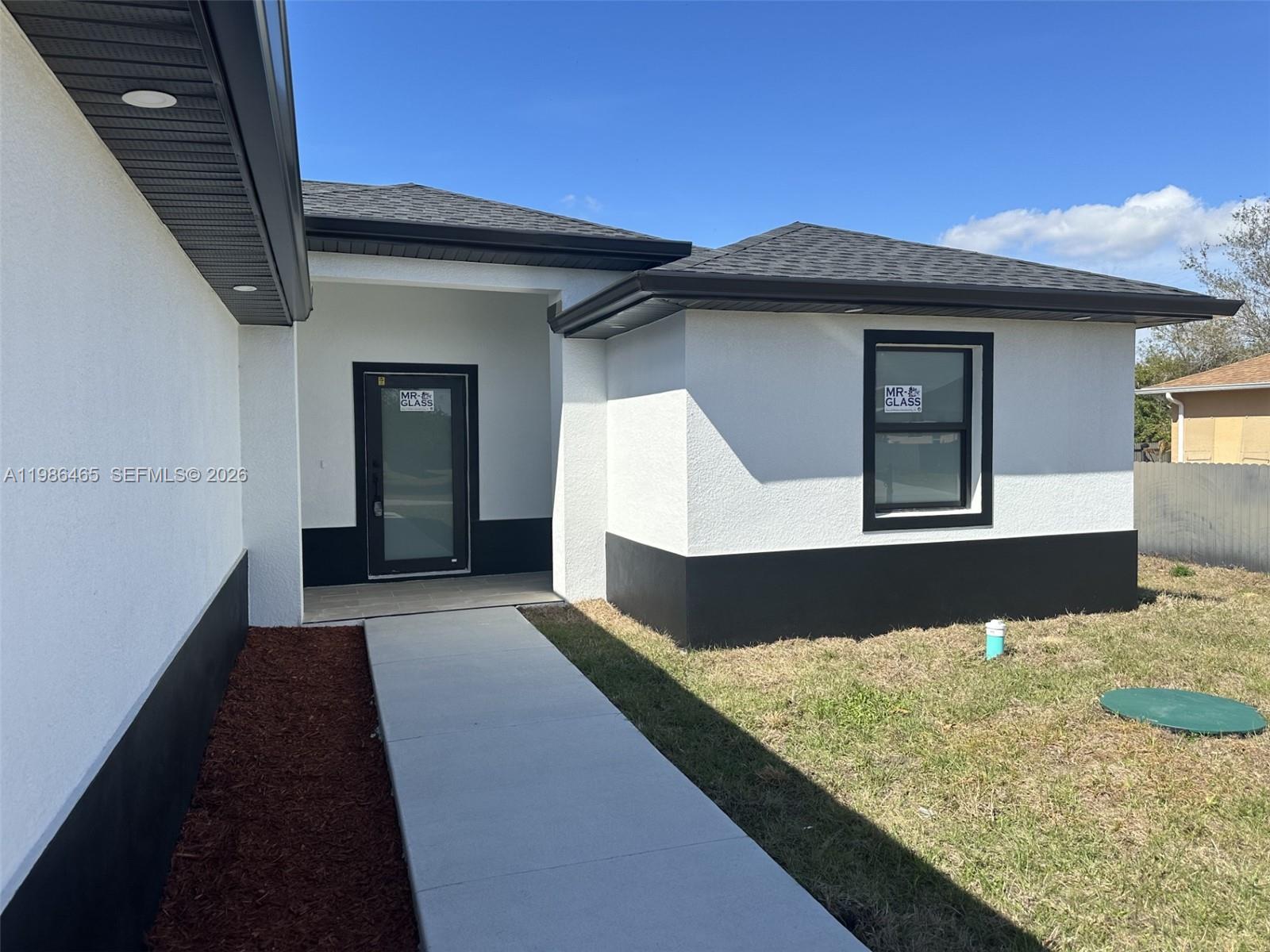 The exterior of a modern house features white stucco walls with black trim and accents — 712 EUSTON AVENUE S, Lehigh Acres FL 33974, LEHIGH ACRES, FL