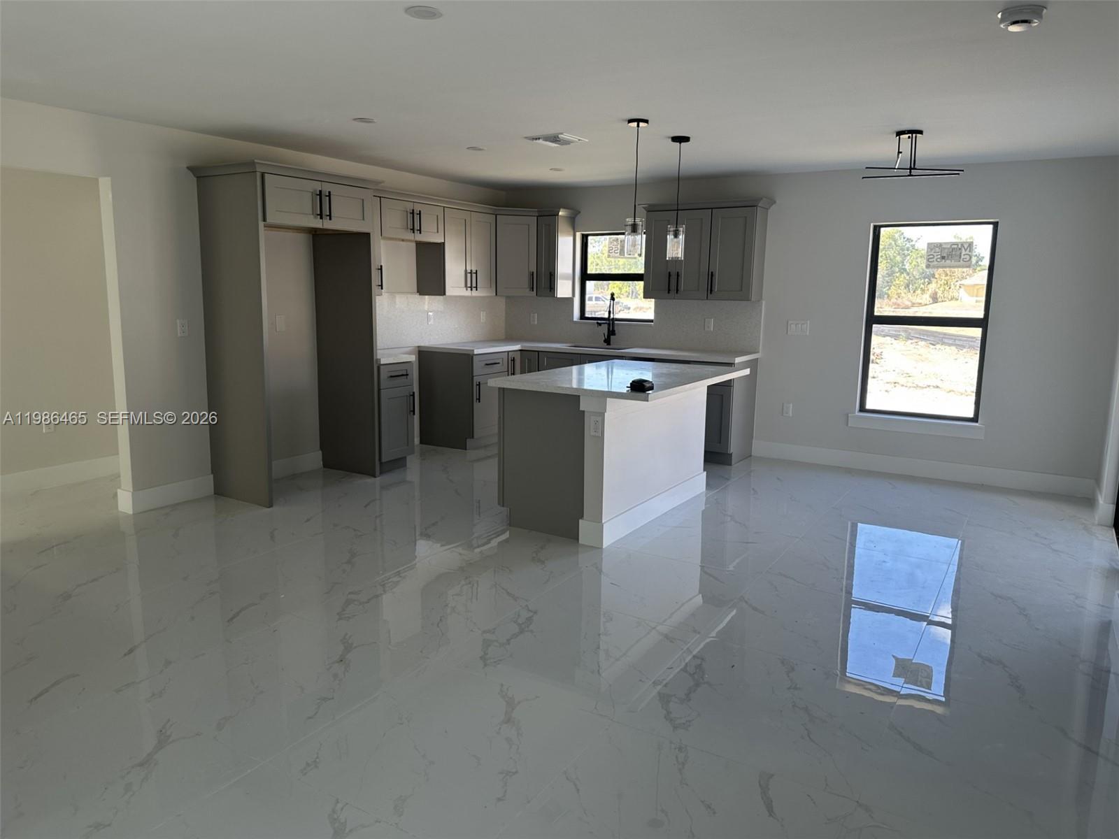 A modern kitchen features grey cabinetry, a white island, and polished marble-look tile flooring — 712 EUSTON AVENUE S, Lehigh Acres FL 33974, LEHIGH ACRES, FL