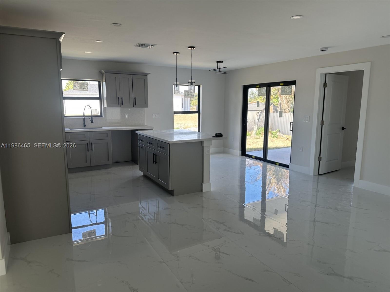 A modern kitchen features gray cabinetry, a central island, and white marble-look tile flooring — 712 EUSTON AVENUE S, Lehigh Acres FL 33974, LEHIGH ACRES, FL