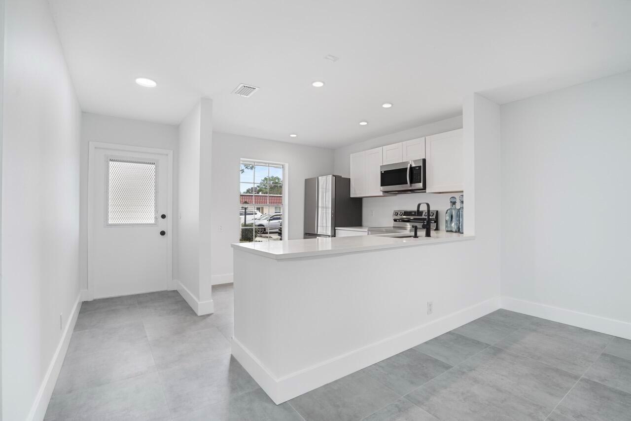 A bright kitchen features white cabinets, stainless steel appliances, a breakfast bar, and gray flooring — 737 Nantucket Circle # B, Lake Worth FL 33467, LAKE WORTH, FL