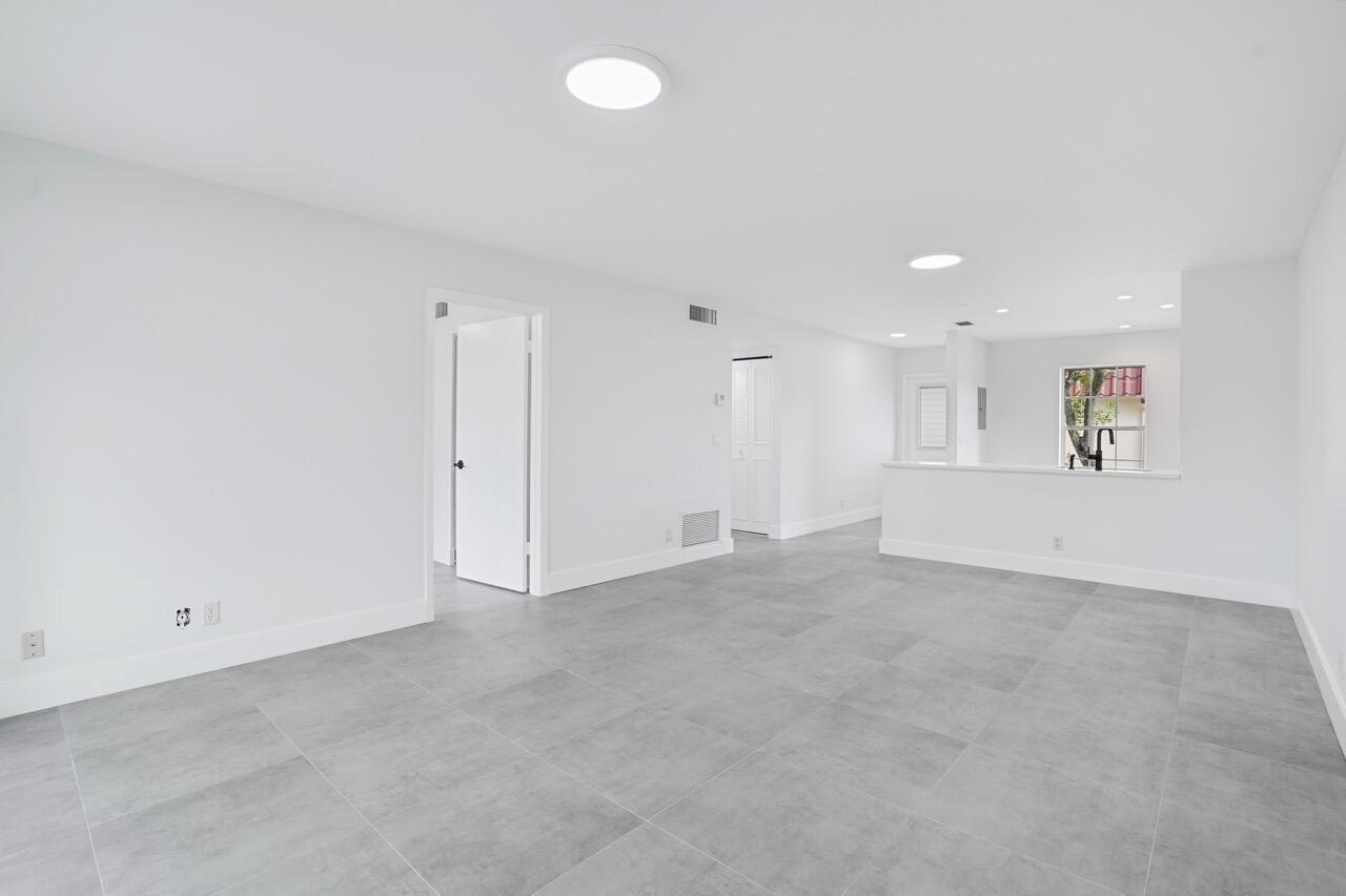 A bright, empty room features gray tile flooring, white walls, and a pass-through kitchen window — 737 Nantucket Circle # B, Lake Worth FL 33467, LAKE WORTH, FL