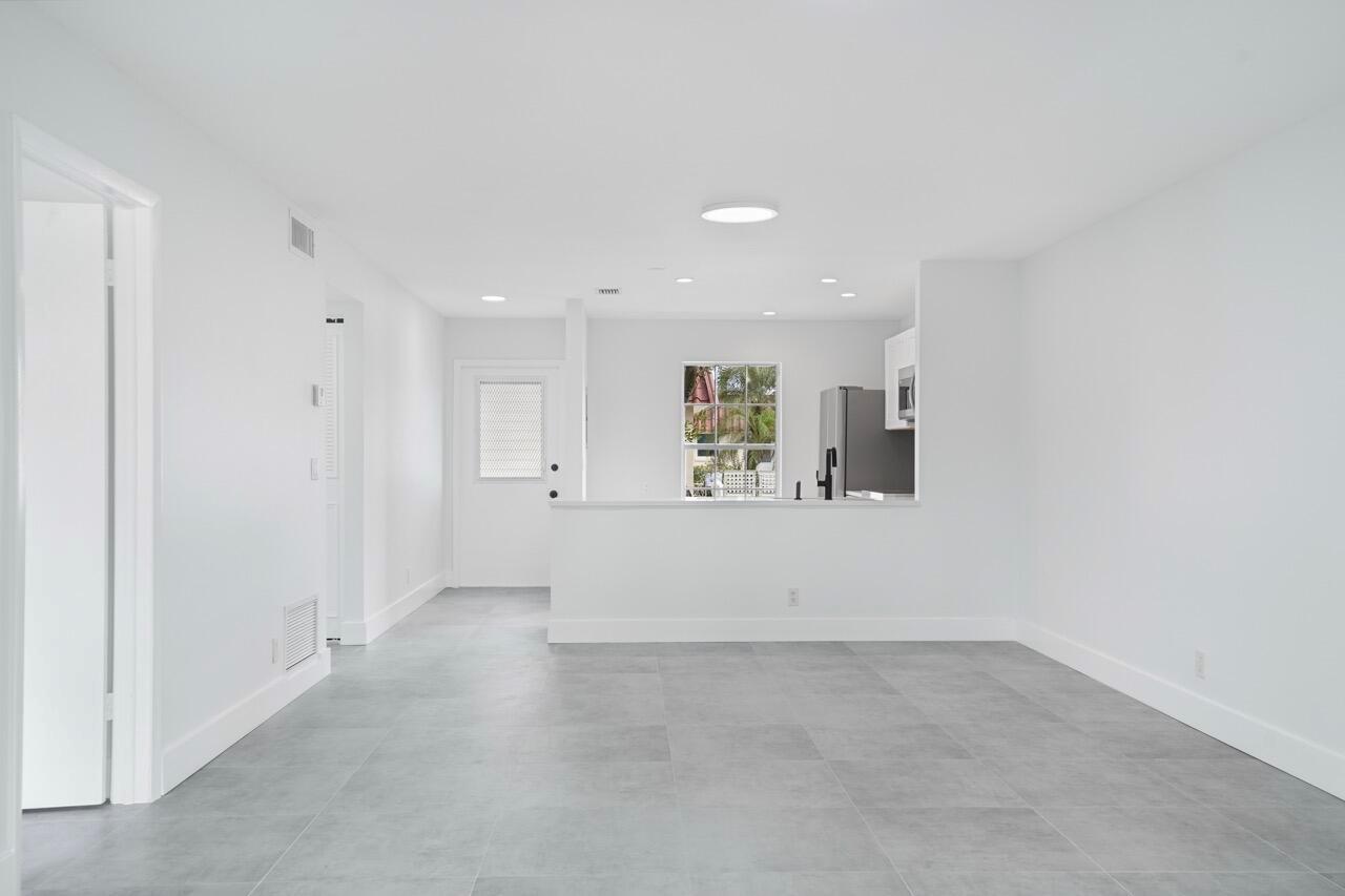 A bright, minimalist living area features white walls, gray tile flooring, and an open kitchen — 737 Nantucket Circle # B, Lake Worth FL 33467, LAKE WORTH, FL
