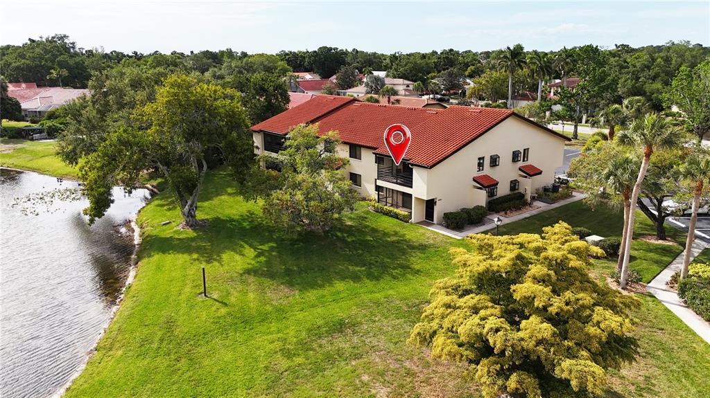 An aerial view shows a two-story apartment building with a red tile roof near water — 5654 GARDENS DRIVE, SARASOTA, FL