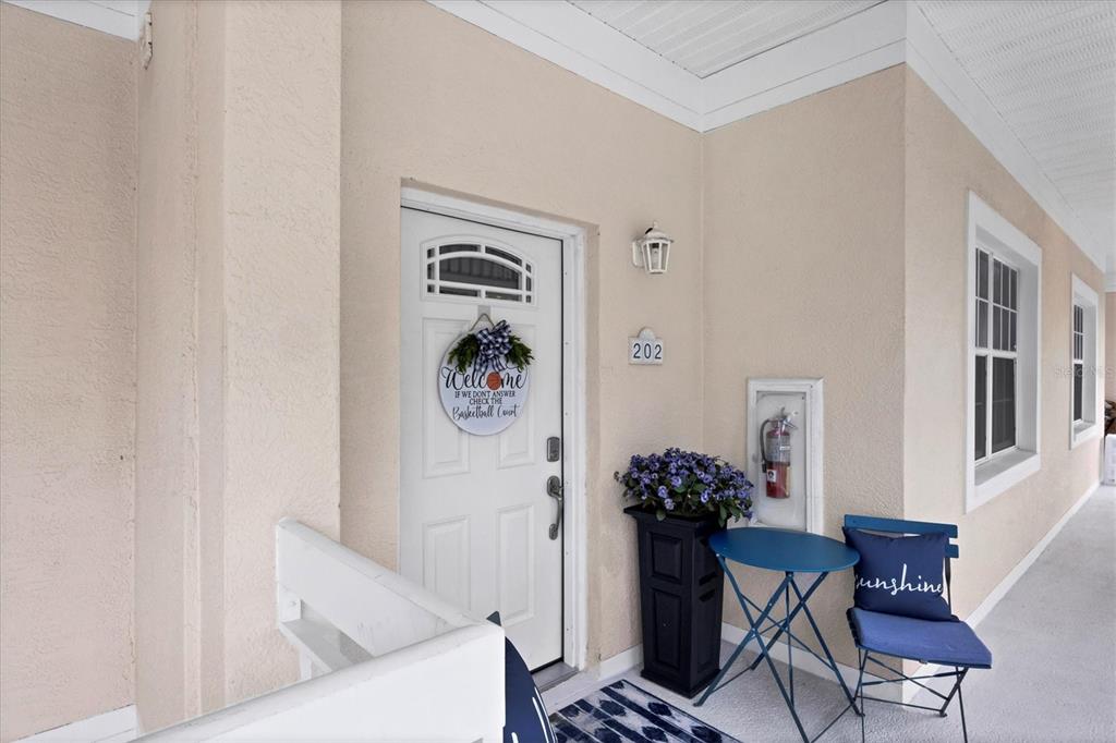 A covered entryway features a white front door with a welcome sign and a small patio set — 3701 54TH DRIVE W UNIT 202, BRADENTON, FL