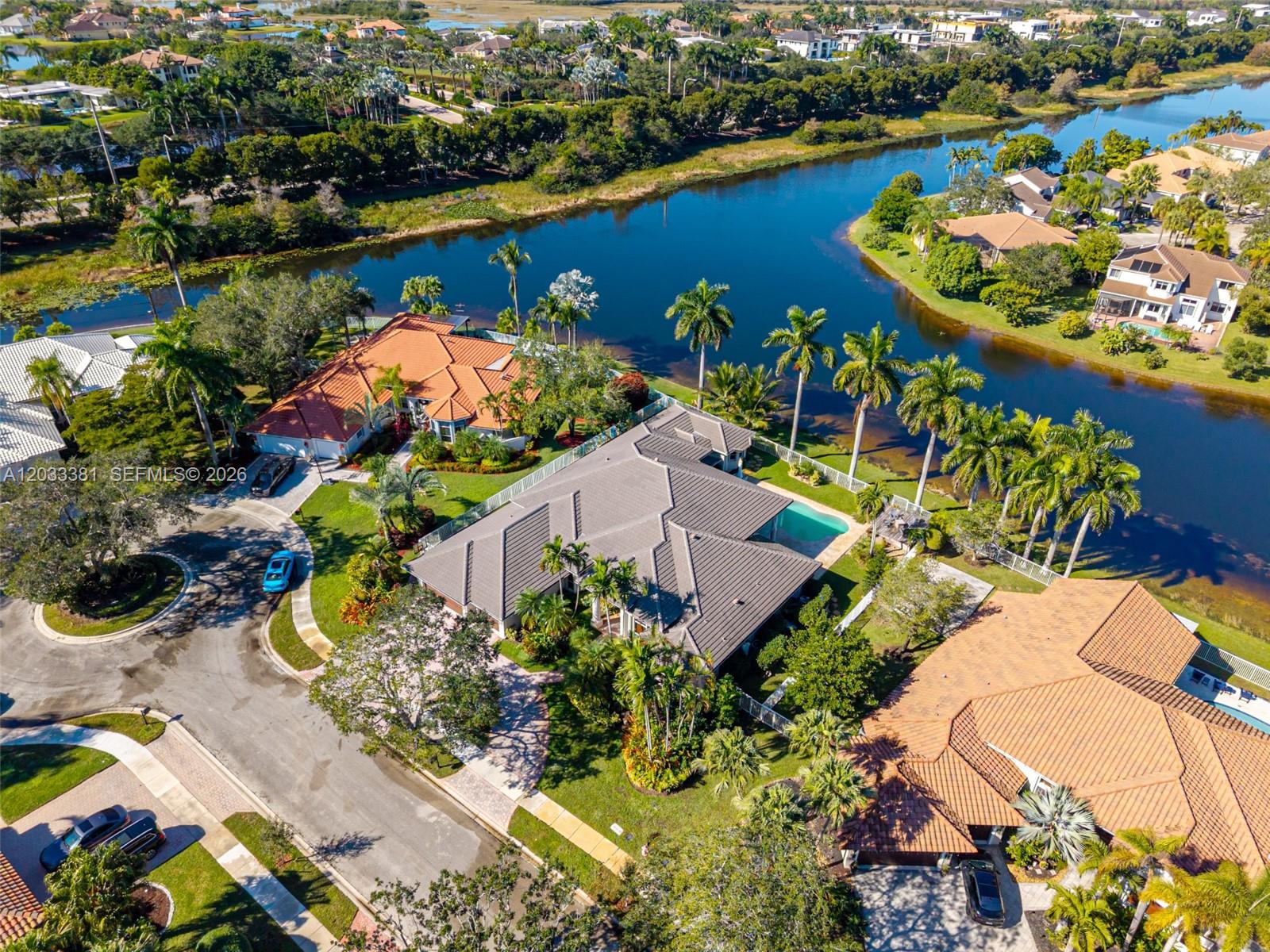 An aerial view shows several houses with tiled roofs, swimming pools, and palm trees near water — 2950 Medinah, Weston FL 33332, WESTON, FL