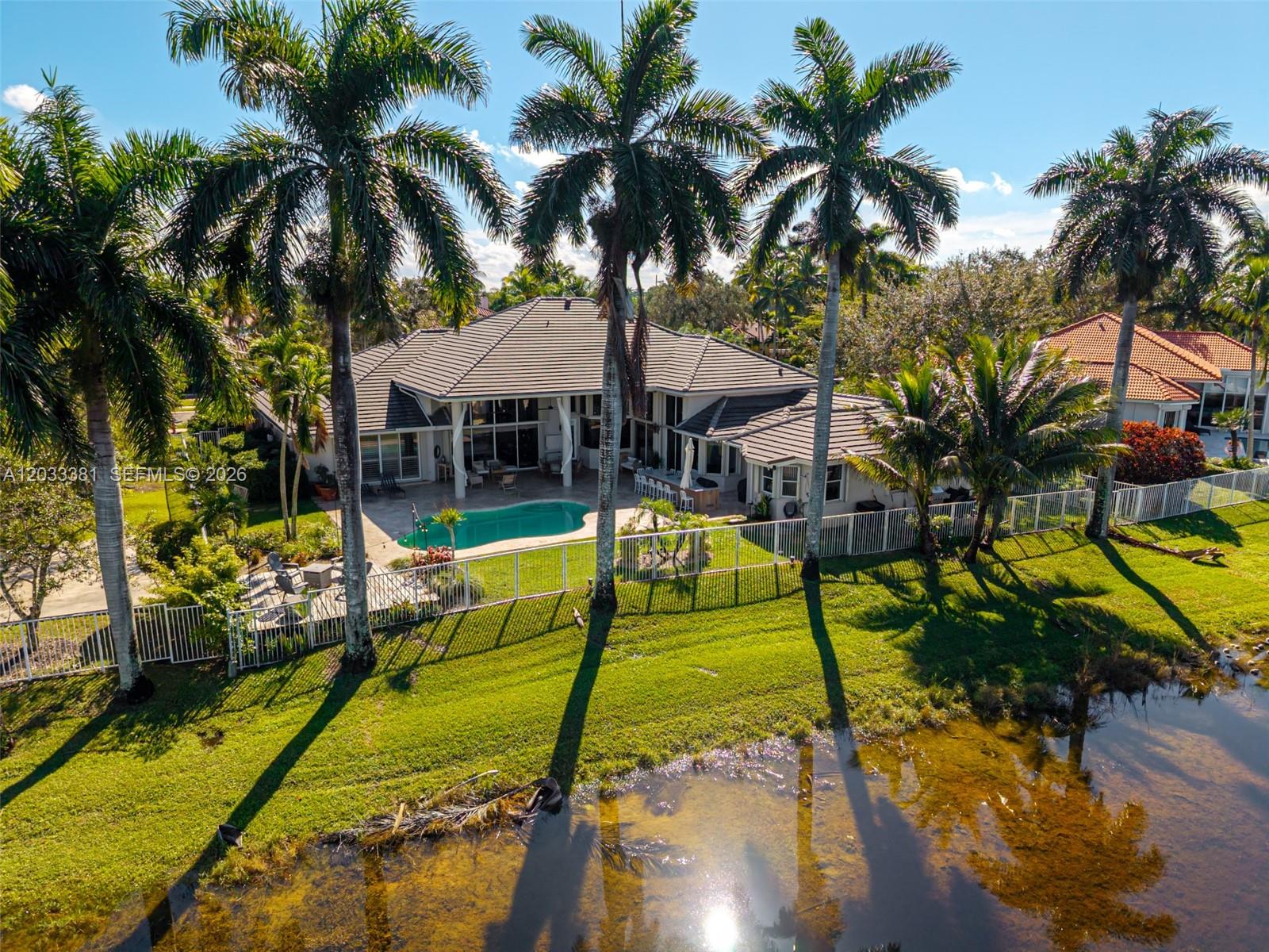 An aerial view shows a house with a pool, patio, and palm trees by a lake — 2950 Medinah, Weston FL 33332, WESTON, FL