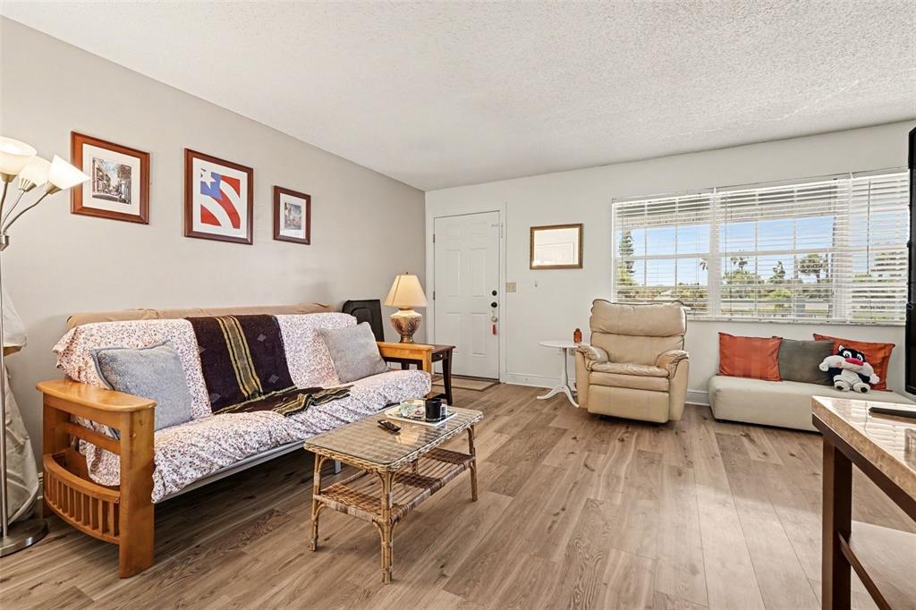 A living room features wood-look flooring, a futon, a recliner, and a window with blinds — 1011 S MIRAMAR AVENUE UNIT 9, INDIALANTIC, FL