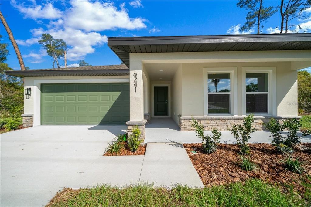 A single-story house features a green garage door, stone accents, and a covered entryway — 6241 FREEPORT DRIVE, SPRING HILL, FL