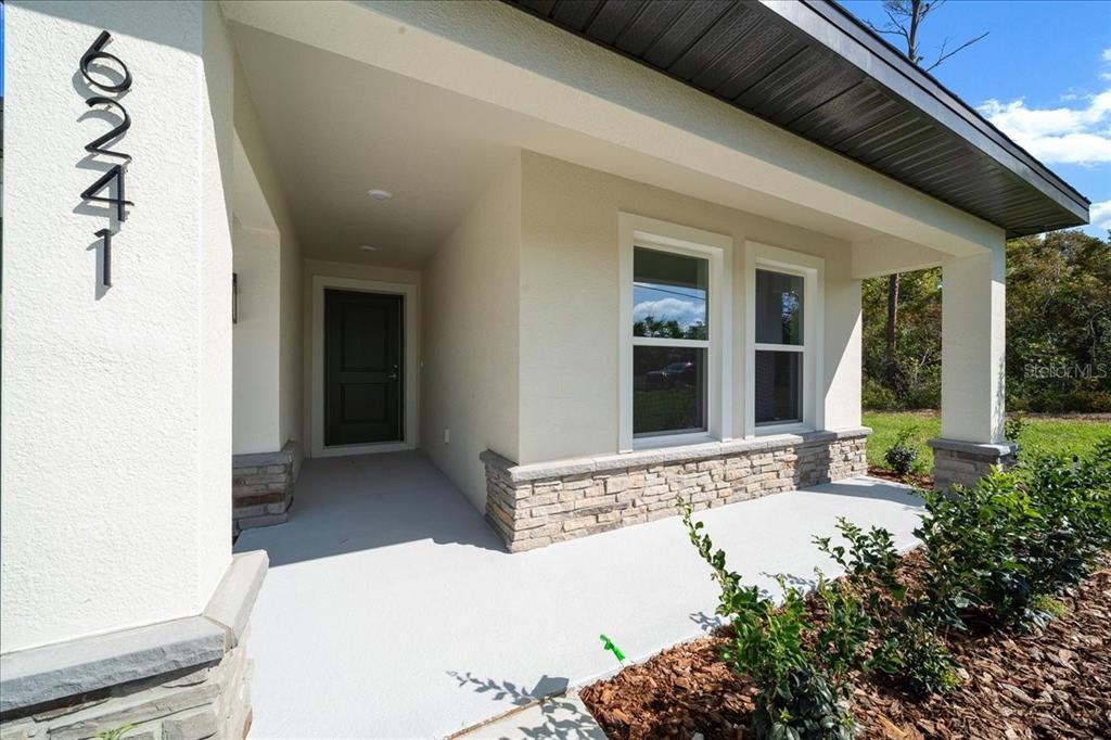 A covered front porch features a concrete floor, stone accents, and a dark front door — 6241 FREEPORT DRIVE, SPRING HILL, FL