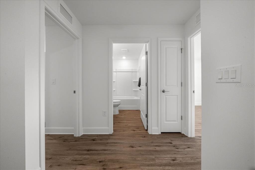 A hallway with wood-look flooring leads to a bathroom and two doorways in a home — 6241 FREEPORT DRIVE, SPRING HILL, FL