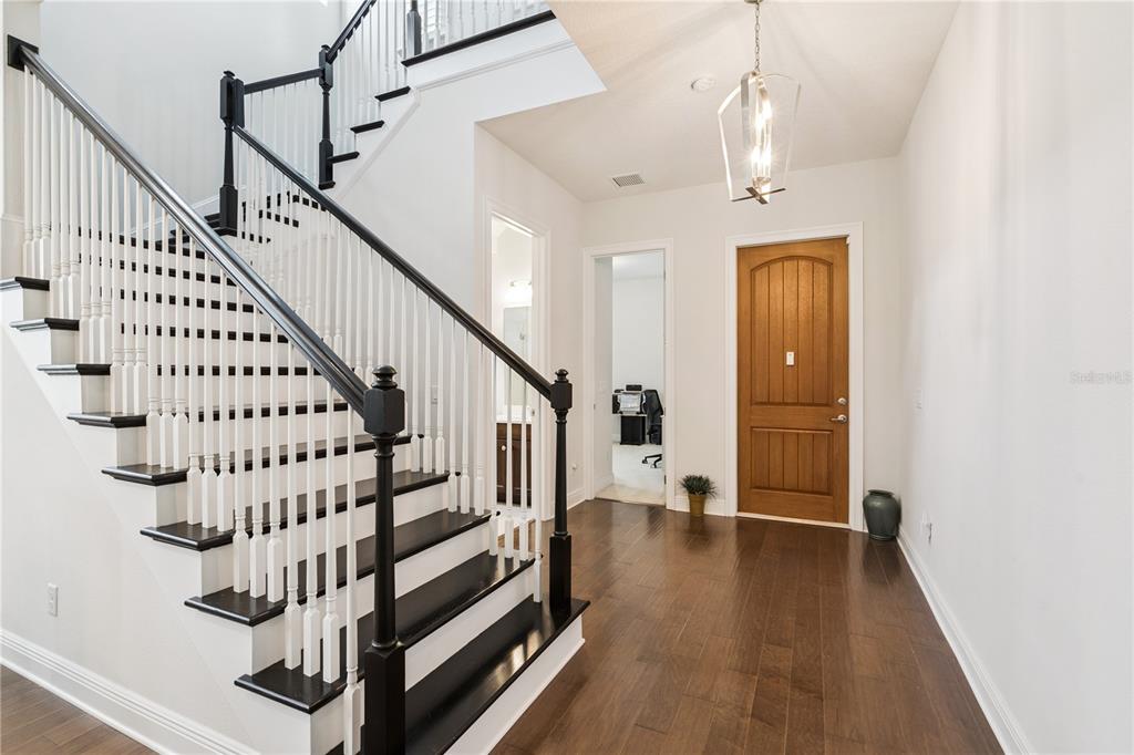 An entryway features a dark wood staircase with white balusters, hardwood floors, and a front door — 15709 SHOREBIRD LANE, WINTER GARDEN, FL
